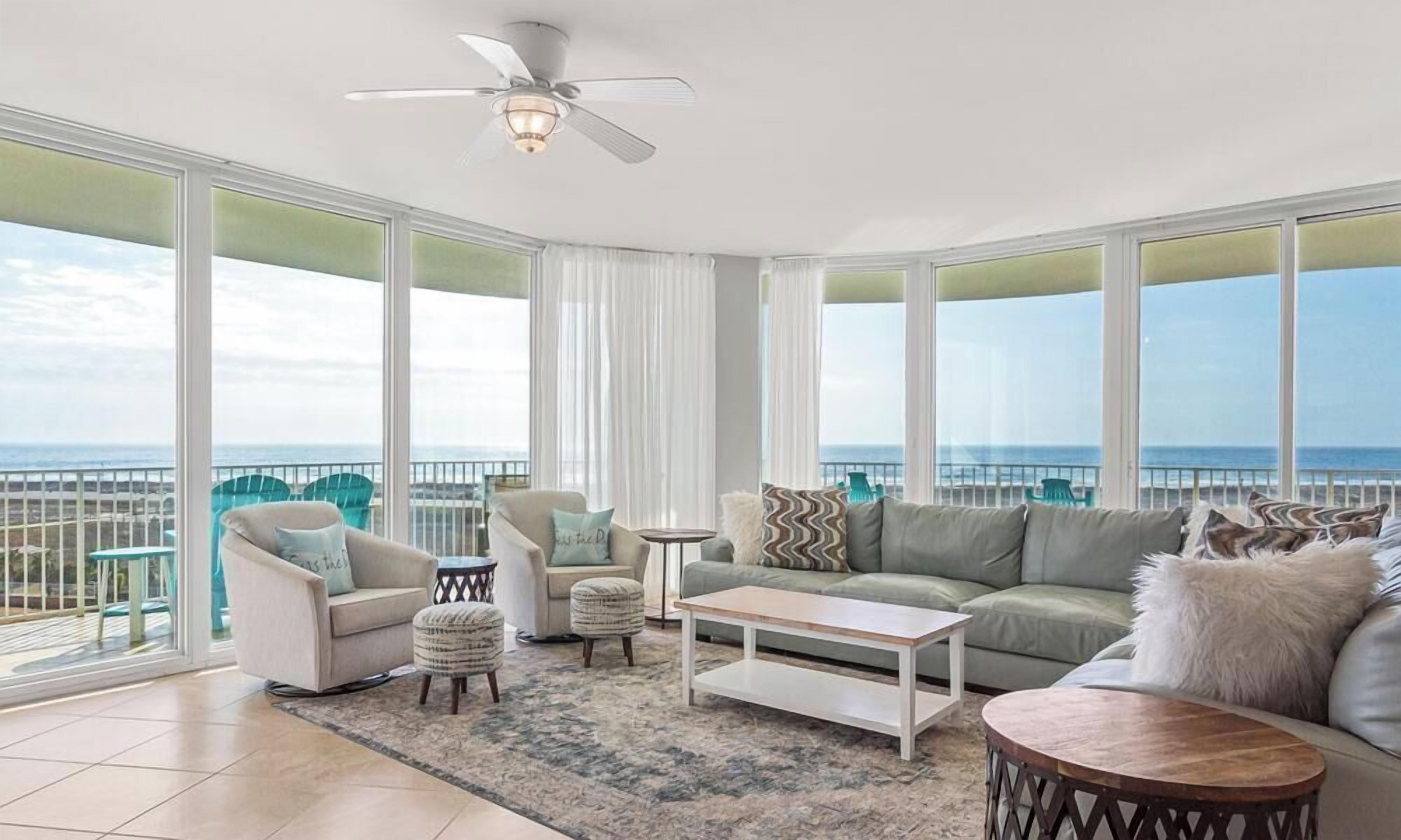 A spacious living room with a large balcony, a ceiling fan, and a view of the ocean.
