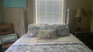 A bedroom with a floral bedspread, a starfish pillow, a wooden headboard, a lamp, and a window with blinds. - Coastal Charm!!!! Super cute and clean!! (Port St Joe)