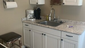 A kitchen with white cabinets, a granite countertop, a coffee maker, a sink, and a hanging pot rack. - Coastal Charm!!!! Super cute and clean!! (Port St Joe)