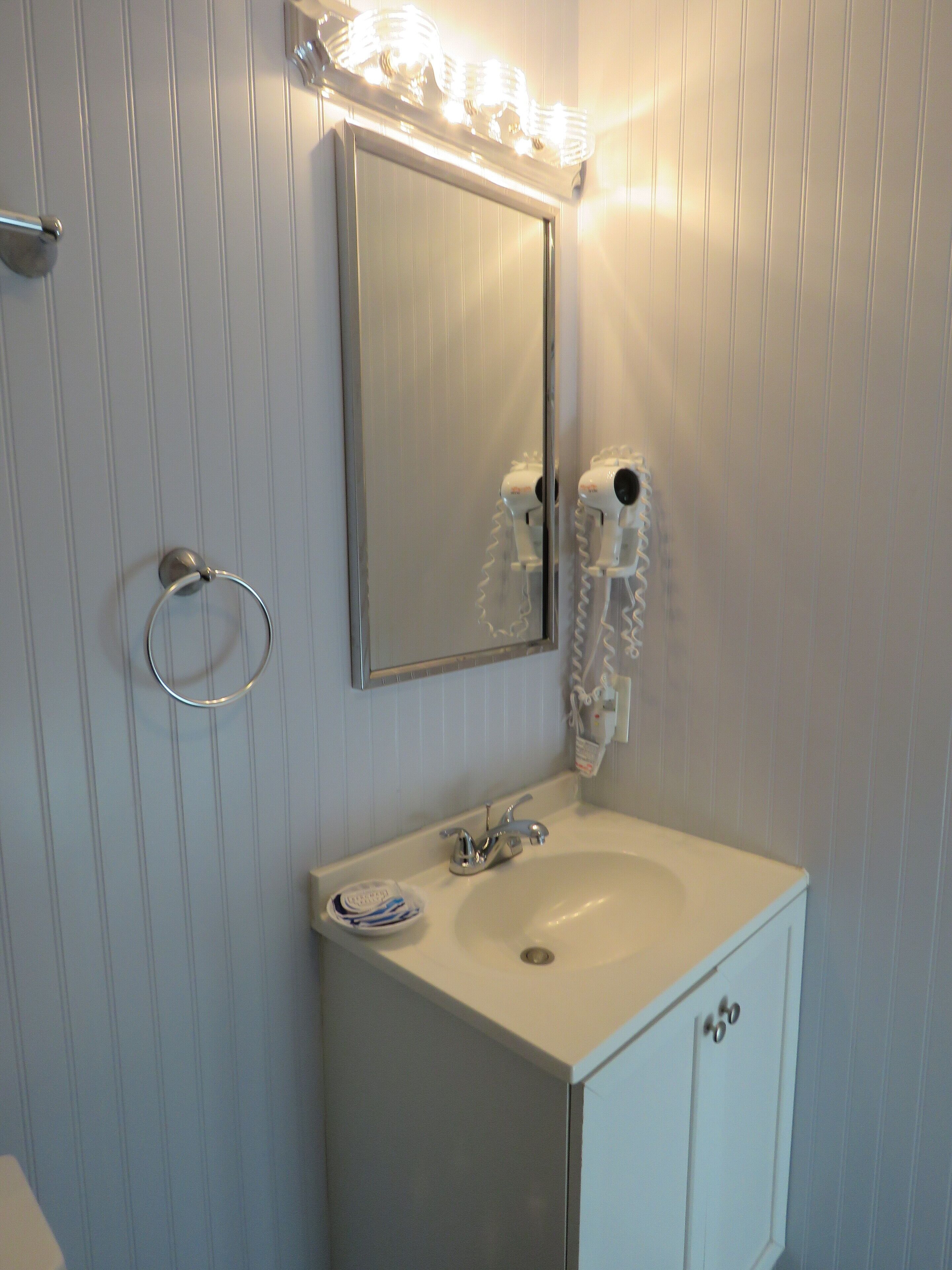 Un bagno con un lavandino bianco, uno specchio e un asciugacapelli montato a parete.