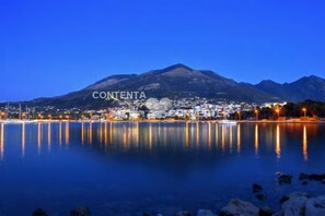 A nighttime view of Contenta, featuring a calm lake reflecting city lights and a mountain in the background.