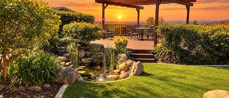 A gazebo with outdoor seating, surrounded by a well-maintained garden with a pond, rocks, and various plants.