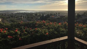 A view from a balcony overlooking a cityscape with a body of water in the distance, a clear sky, and red flowers in the foreground. - Beautiful Ocean View Home Overlooking San Diego Perfect For Your Family Vacation (San Diego)