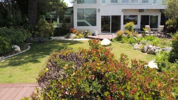 A modern two-story house with large windows, a well-maintained garden with various plants and rocks, and a patio area with outdoor furniture. - Beautiful Ocean View Home Overlooking San Diego Perfect For Your Family Vacation (San Diego)