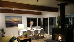 A modern living room with a fireplace, dining area, and a painting of a sunset. - Beautiful Ocean View Home Overlooking San Diego Perfect For Your Family Vacation (San Diego)