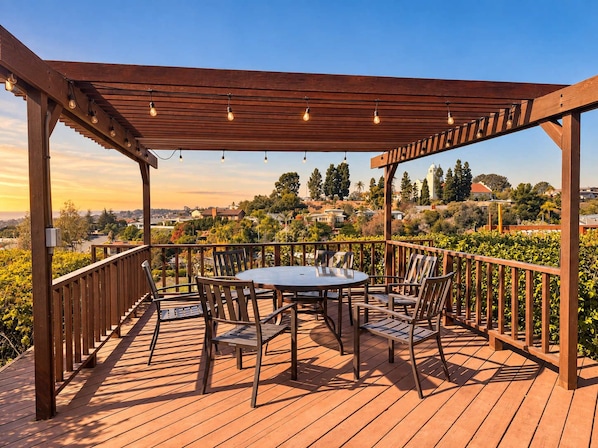 A wooden deck with a pergola, round table, and chairs, overlooking a residential area.