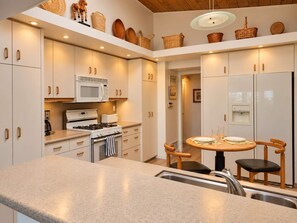A modern kitchen with white cabinetry, a stove, microwave, and a dining area with a table and chairs.