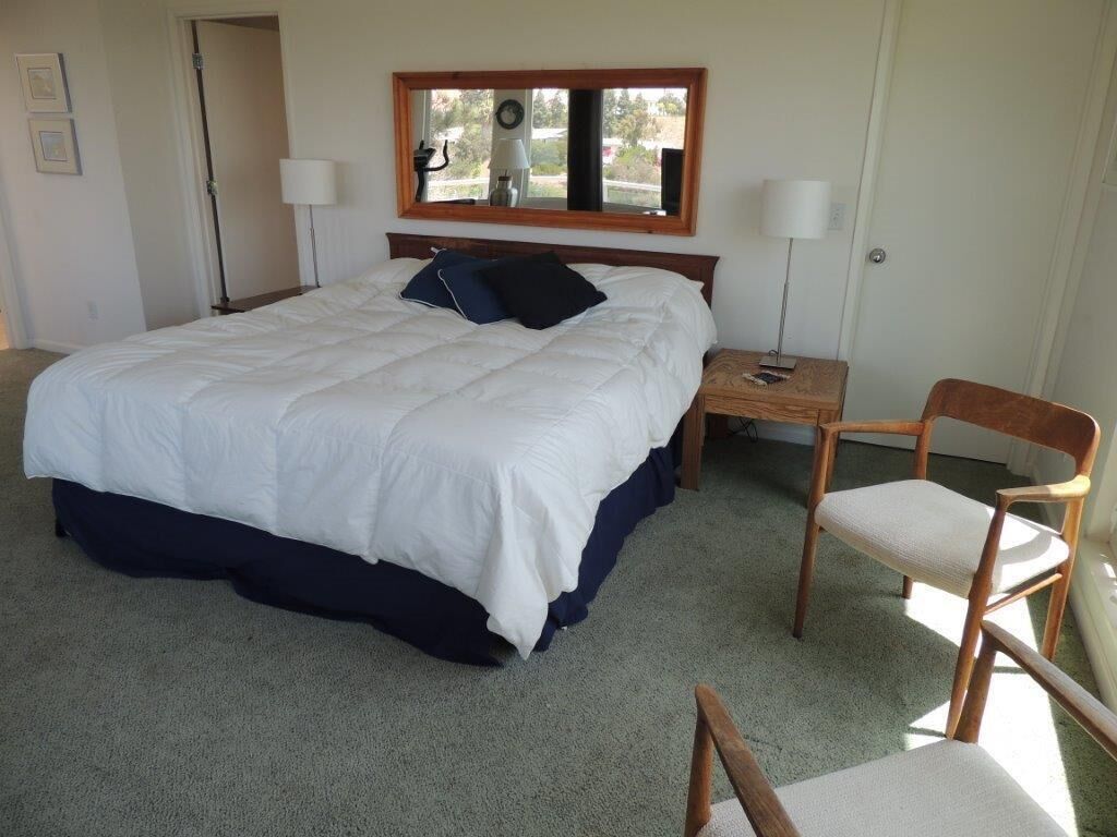 Une chambre à coucher avec un grand lit, une table de chevet en bois, une chaise et un miroir au-dessus du lit.