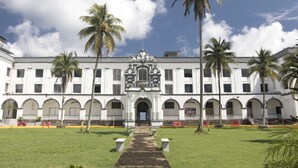 A large white building with a central entrance, surrounded by palm trees and a well-maintained lawn. - New Washington Hotel (Colon)