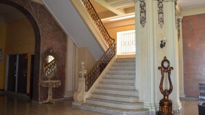 A grand staircase with marble steps and ornate railings, leading to a landing with a large mirror and a decorative table. - New Washington Hotel (Colon)