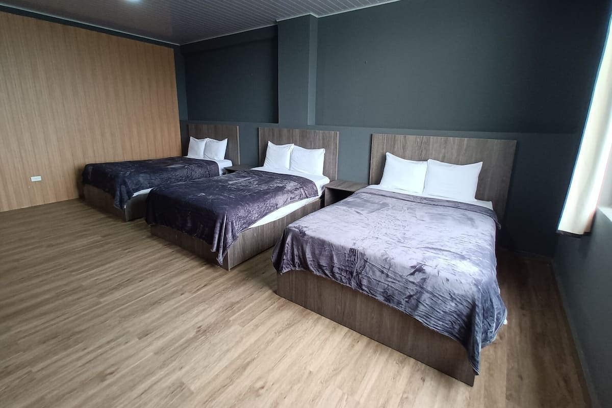 A hotel room with three beds, wooden flooring, and a ceiling with recessed lighting.