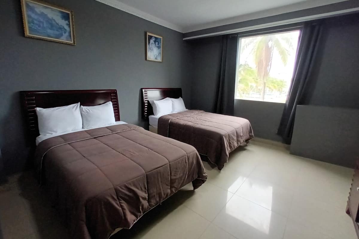 A hotel room with two beds, a large window with curtains, and a painting on the wall.