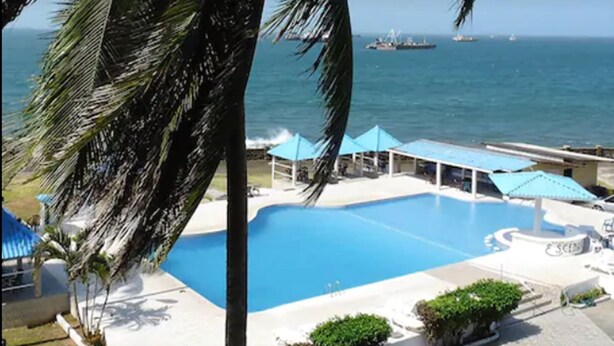 A swimming pool with a view of the ocean and ships in the distance. - New Washington Hotel (Colon)