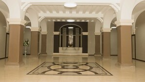 A spacious lobby with a central staircase, flanked by columns and arches, leading to a dark-toned room. - New Washington Hotel (Colon)