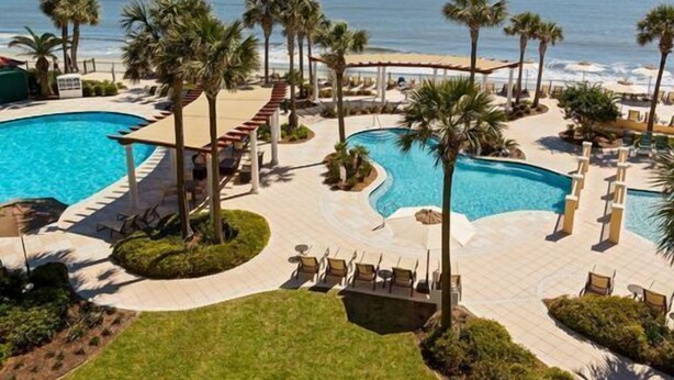 A resort with multiple swimming pools, palm trees, and a beach view. - Family Friendly, King & Prince South Villa with Beach and Resort Amenities (St Simons Island)