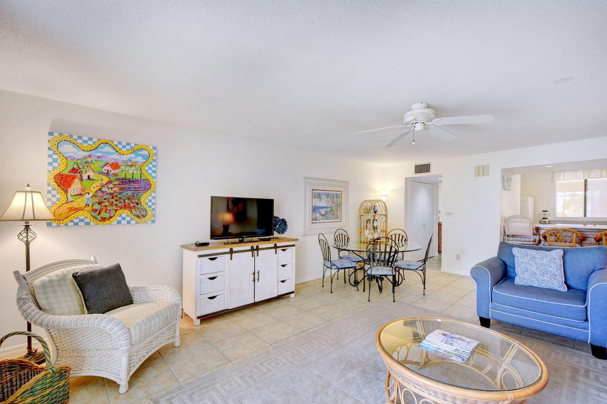 A living room with a television, white wicker furniture, a dining table with chairs, and a ceiling fan.