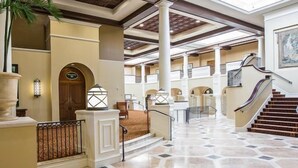 A spacious lobby with a tiled floor, a central staircase, and a large column. - Family Friendly, King & Prince South Villa with Beach and Resort Amenities (St Simons Island)