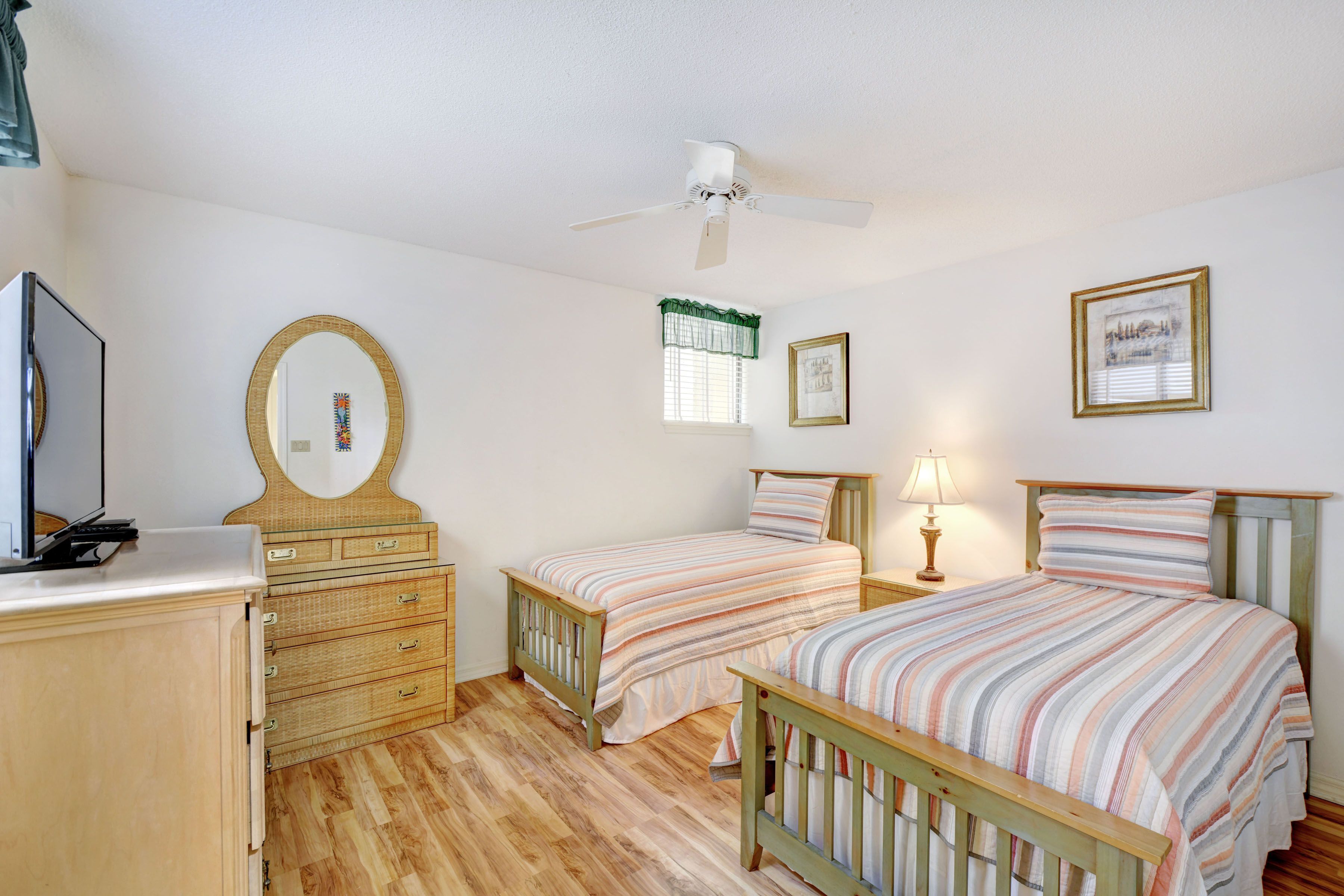 A bedroom with two beds, a dresser, a mirror, a ceiling fan, and a window with curtains.
