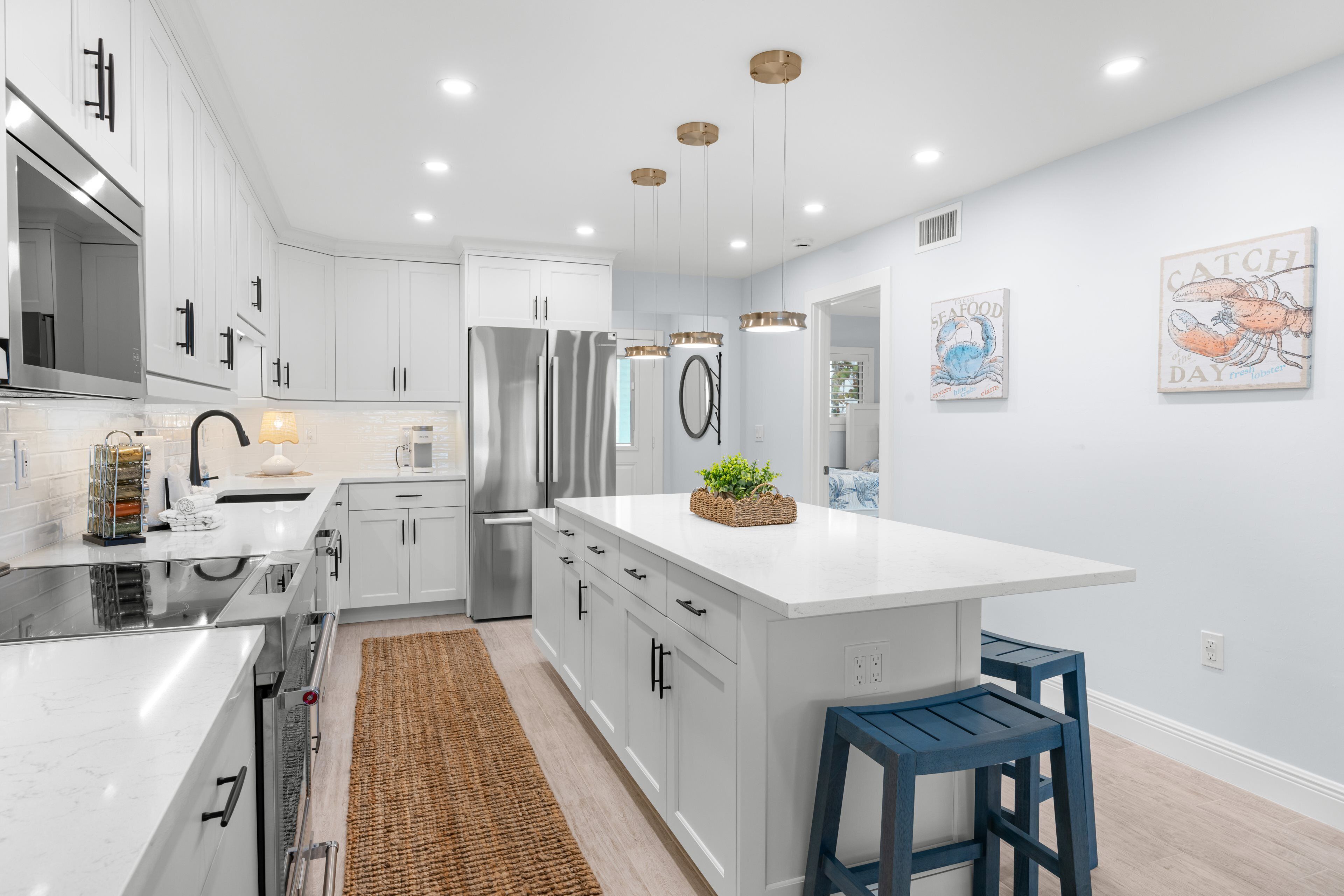 A modern kitchen with white cabinetry, stainless steel appliances, a central island with stools, and artwork on the walls.