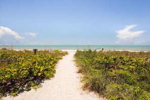 A sandy beach path leading to the ocean with lush greenery on either side.