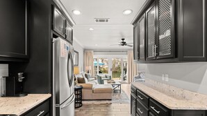 Una cocina moderna con armarios negros, un refrigerador y una cafetera. Hay una zona de estar con un sofá y una mesa de centro.
