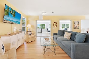 A living room with a glass coffee table, a grey sofa, a beige sofa, a white cabinet, and a painting of a beach scene. - Beautiful 5 Bedroom Captiva Pool Home Central to Stunning Beaches (Captiva)
