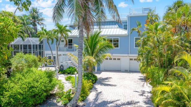 A coastal house with a paved driveway, palm trees, and a clear blue sky. - Beautiful 5 Bedroom Captiva Pool Home Central to Stunning Beaches (Captiva)
