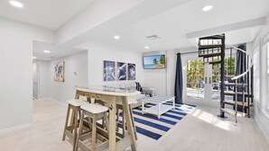 A spacious living room with a wooden table and stools, a sofa, and a TV mounted on the wall. - Beautiful 5 Bedroom Captiva Pool Home Central to Stunning Beaches (Captiva)