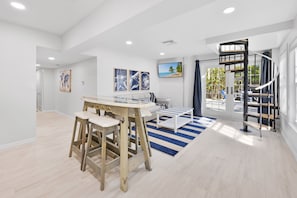 A spacious living room with a wooden table and stools, a sofa, and a TV mounted on the wall. - Beautiful 5 Bedroom Captiva Pool Home Central to Stunning Beaches (Captiva)