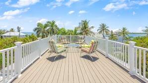 A wooden deck with white railings, two striped lounge chairs, and a view of the sea and palm trees. - Beautiful 5 Bedroom Captiva Pool Home Central to Stunning Beaches (Captiva)