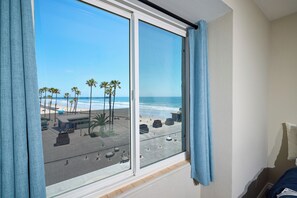 A room with a large window overlooking a beach, featuring palm trees and a clear sky.