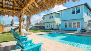 A backyard with a swimming pool, a covered patio, and a two-story house. - Coastal Chic Cottage w/ View of Community Pool! (Port Aransas)