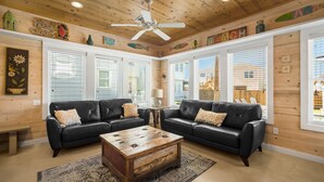 A living room with two black leather sofas, a wooden coffee table, and a ceiling fan. - Coastal Chic Cottage w/ View of Community Pool! (Port Aransas)