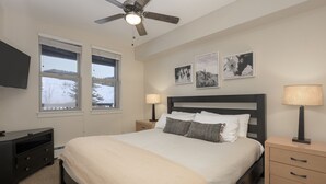 Une chambre à coucher comprenant un lit, deux tables de chevet, un ventilateur de plafond, un téléviseur et trois tableaux encadrés accrochés au mur.