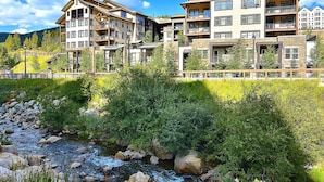 Un hôtel à plusieurs étages doté de balcons, avec une rivière au premier plan et des montagnes en arrière-plan.