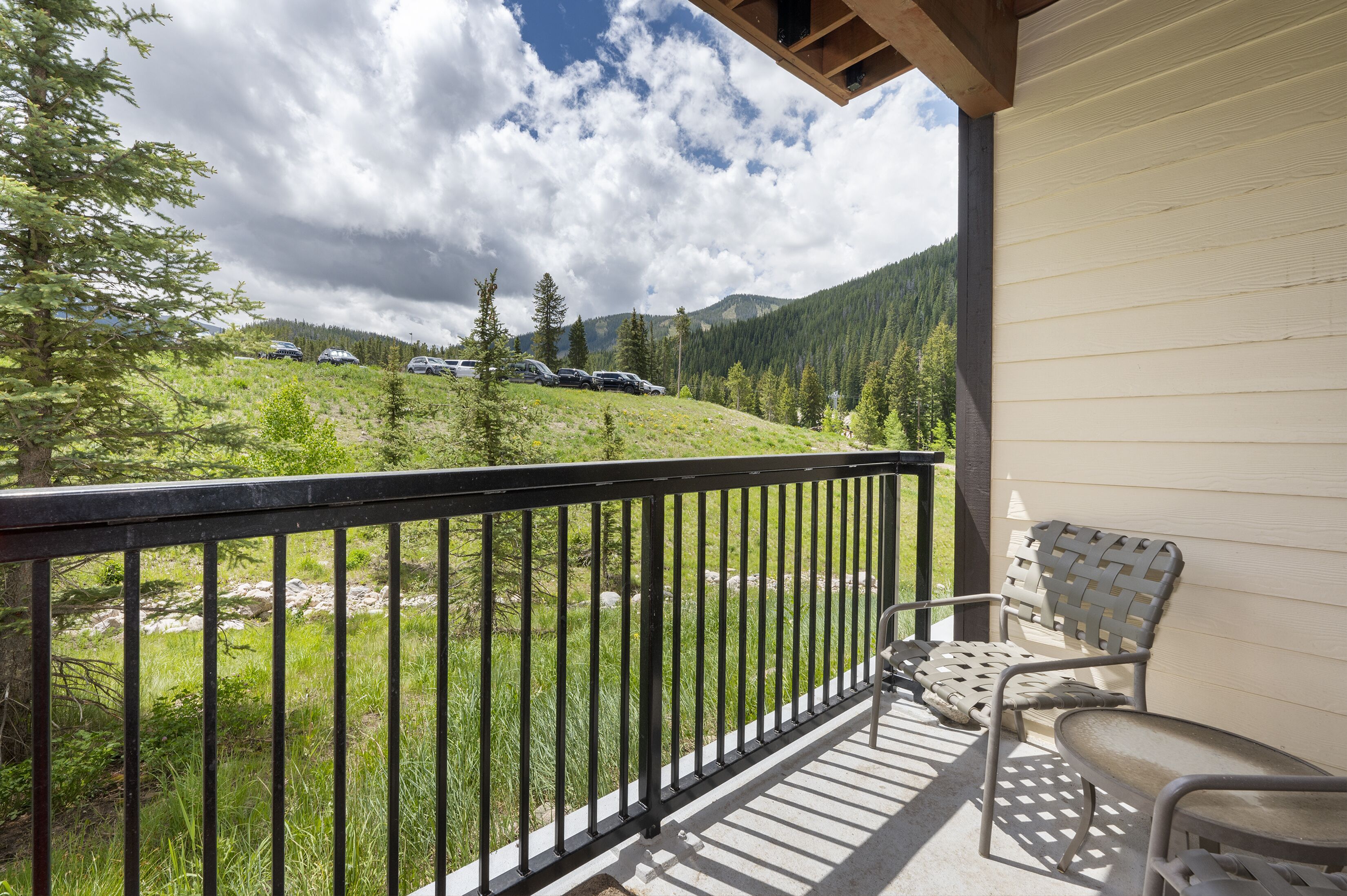 A balcony with a view of a grassy hillside and parked cars.
