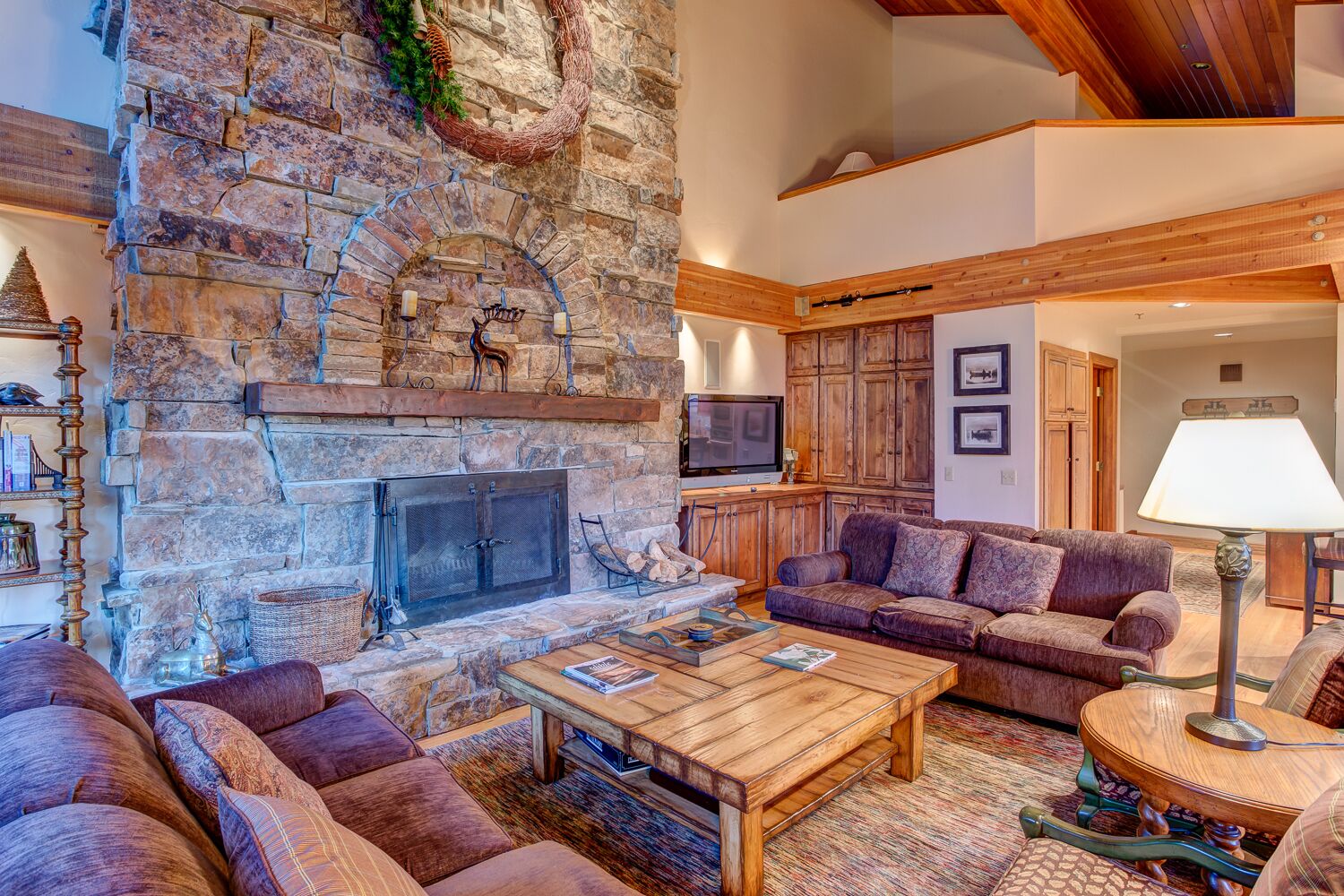 A cozy living room with a stone fireplace, wooden furniture, and a television.