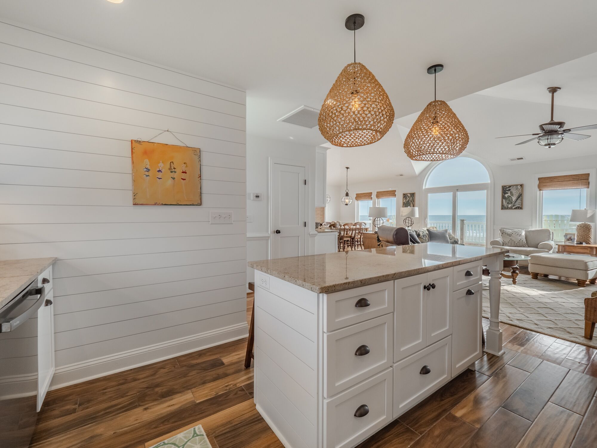 A spacious kitchen with white cabinetry, a large island, and hanging wicker pendant lights.