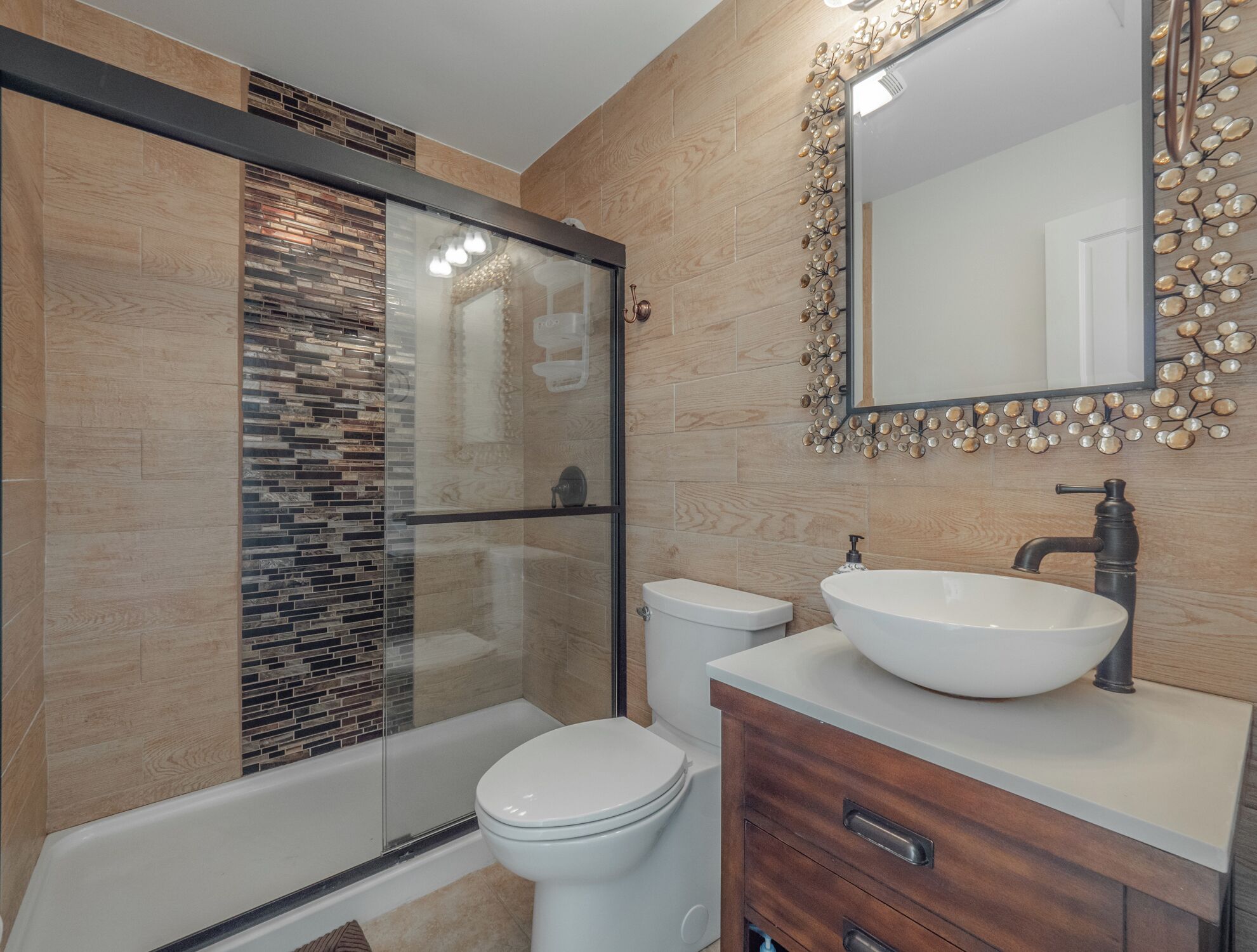 A modern bathroom with a glass shower enclosure, a white toilet, and a wooden vanity with a large mirror.