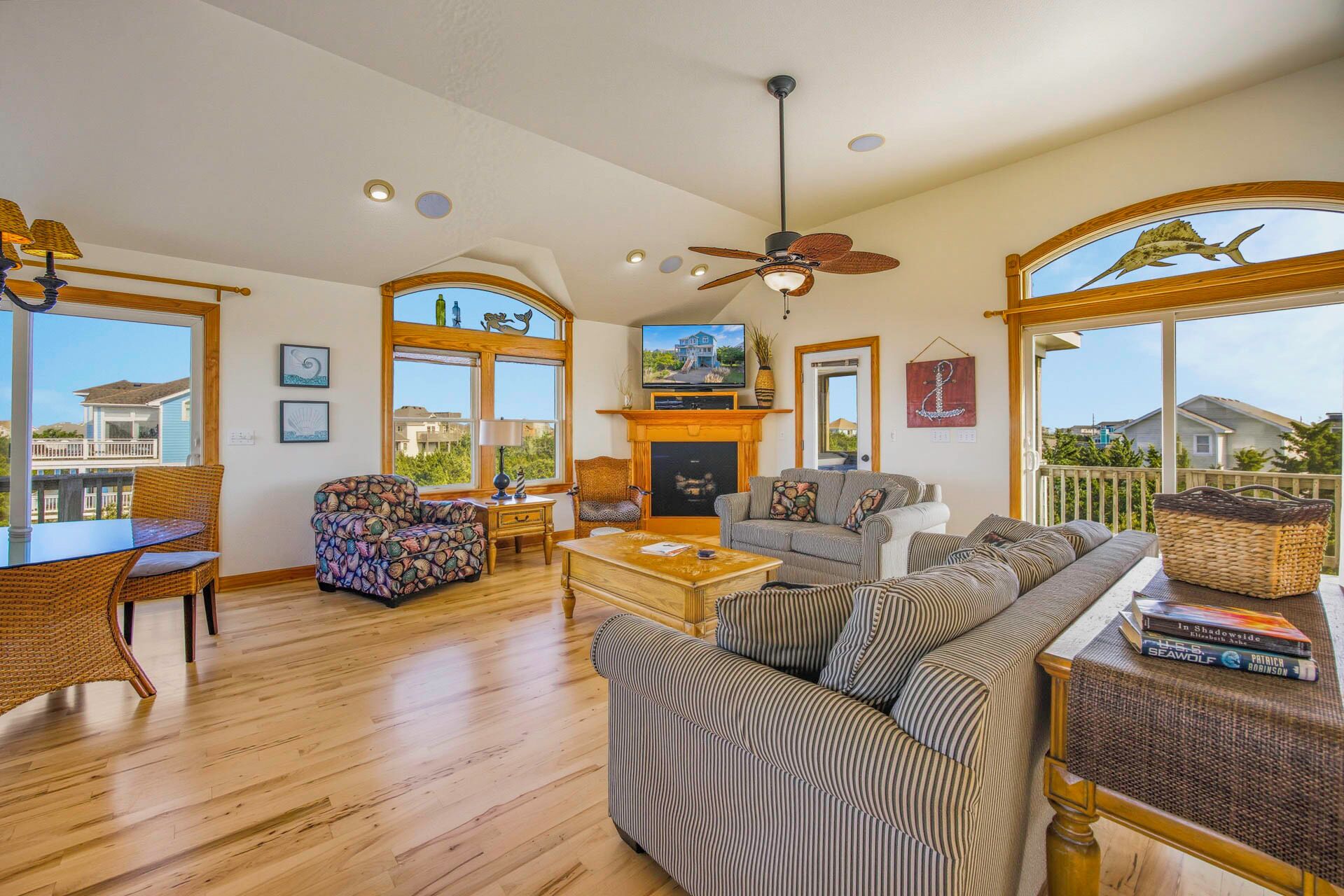 A spacious living room with a fireplace, large windows, and a ceiling fan.