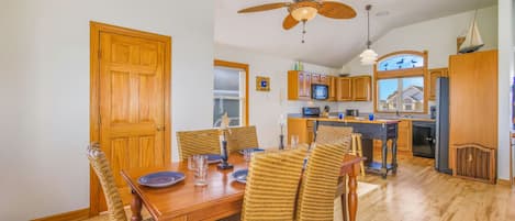 A dining area with a wooden table and wicker chairs, a kitchen with wooden cabinets and a black refrigerator, and a ceiling fan.