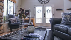 Una sala de estar con una pared de piedra, un sofá de cuero negro, una mesa de centro con un jarrón y velas, y un reloj en la pared.