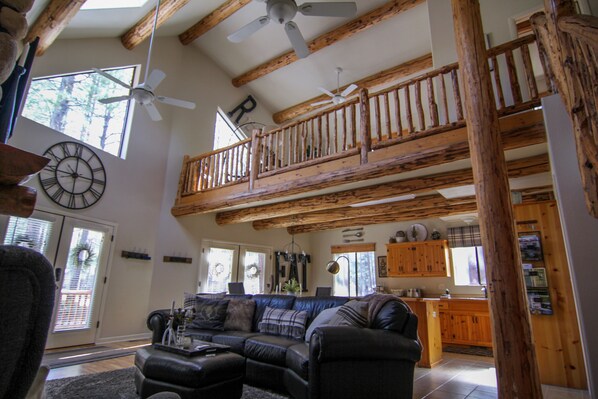 A spacious living room with a large couch, a wooden balcony, and a kitchen area.