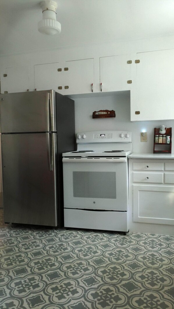 A kitchen with a stainless steel refrigerator, a white oven, and a white cabinet with a wooden shelf above.
