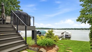 A waterfront property with a covered outdoor area, steps leading to a deck, and a dock with a boat. - MINNeSTAY* Lakefront Luxury (Mound)