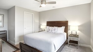 Un dormitorio con cama, mesita de noche con lámpara, ventilador de techo y cómoda.