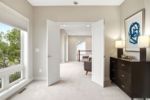 A hallway with a large window, a dark wooden dresser, and a framed abstract painting.