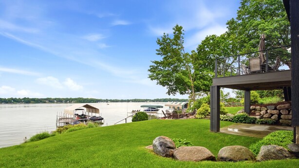 Una propiedad frente al lago con un muelle techado, una terraza con asientos y un muro de piedra.