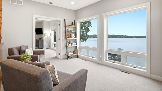 A spacious living room with a large window overlooking a lake, a fireplace, and a bookshelf. - MINNeSTAY* Lakefront Luxury (Mound)