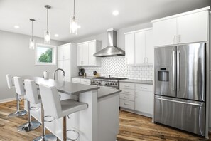 Une cuisine moderne avec des meubles blancs, des appareils en acier inoxydable et des luminaires suspendus.